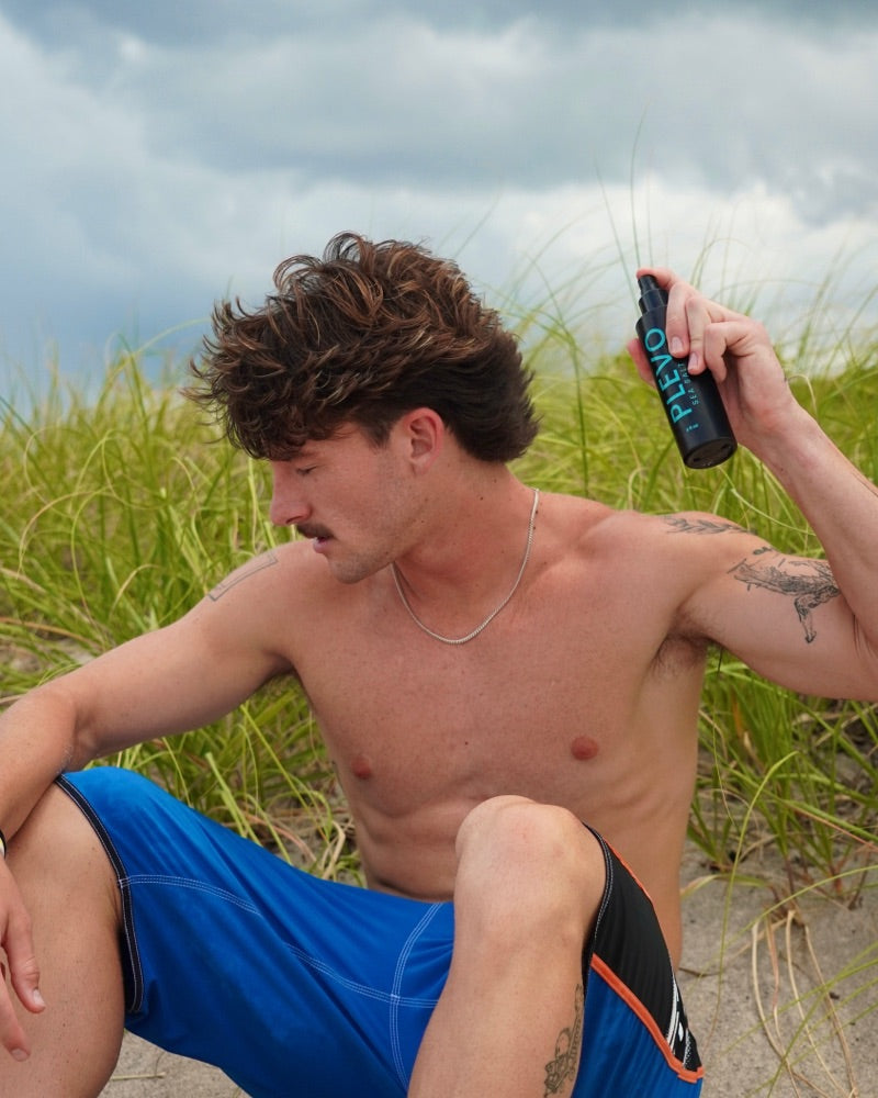 James sitting in the dune grass under an overcast sky, spraying it into his hair