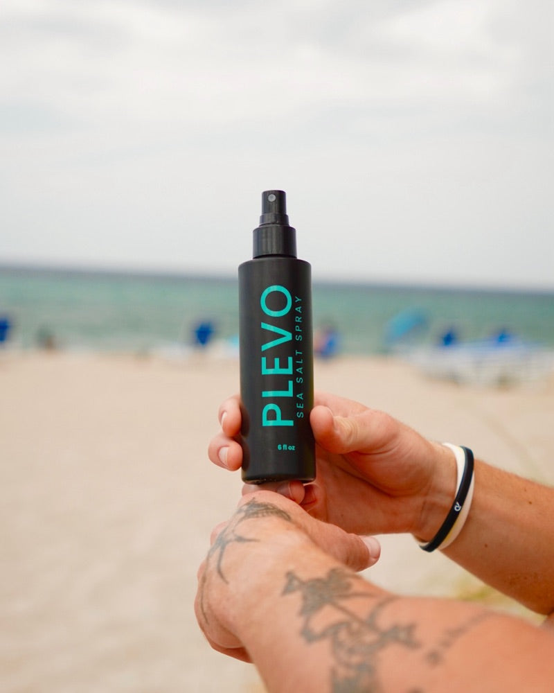 The bottle held in one hand on an overcast day, the beach behind