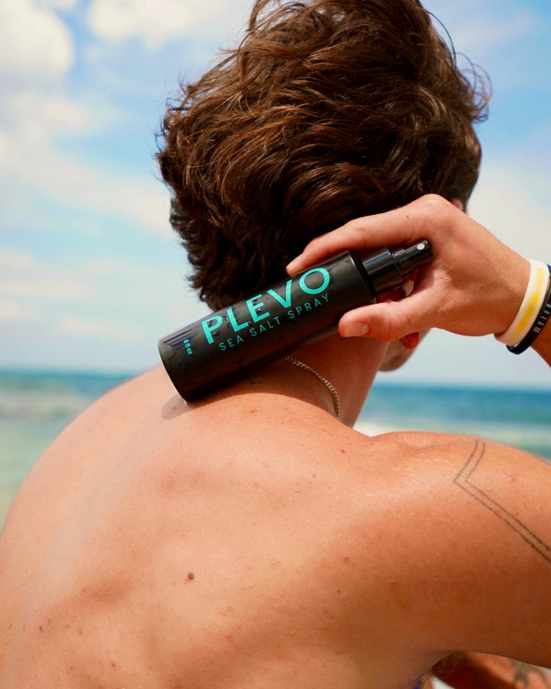 Sitting on the sand, working the spray into dry hair with one hand