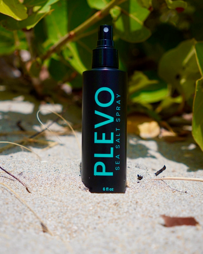 The PLEVO bottle standing upright in dry sand at the foot of coastal dune grass